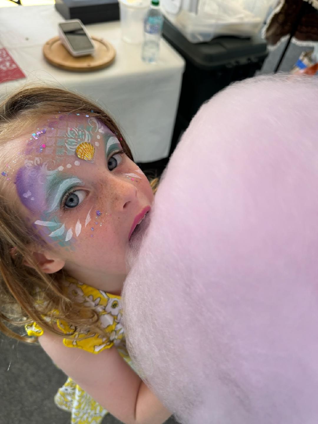 Girl with mermaid face paint biting cotton candy