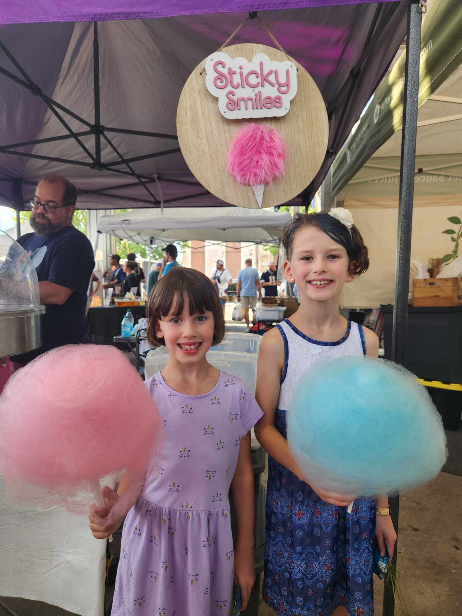 Two girls holding pink and blue cotton candy under the Sticky Smiles sign